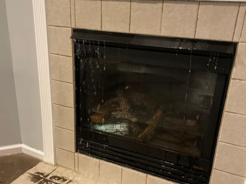 Water leaking down the glass front of a tiled fireplace with a wet floor nearby.