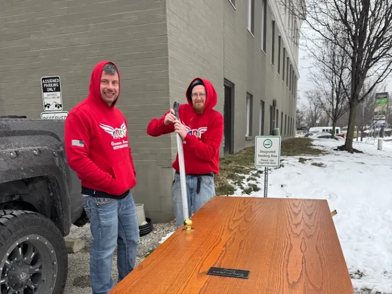 Two men in red hoodies stand outside near a large wooden door on a snowy day.