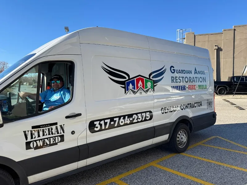 White van with "Guardian Angel Restoration" and contact details parked with a man in a blue shirt sitting inside.