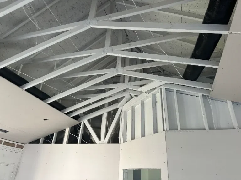 White painted roof trusses and partially finished drywall interior under construction.