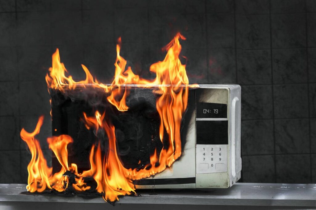 A microwave oven engulfed in bright orange flames on a countertop.
