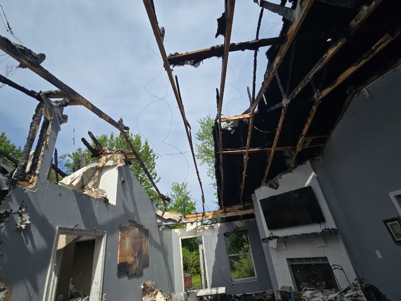 Interior of a house with a severely damaged roof and charred wooden beams exposed.