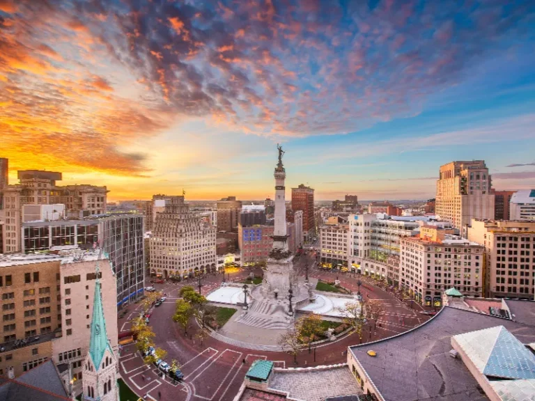 Downtown cityscape with a tall monument in the center under a colorful sunset sky.
