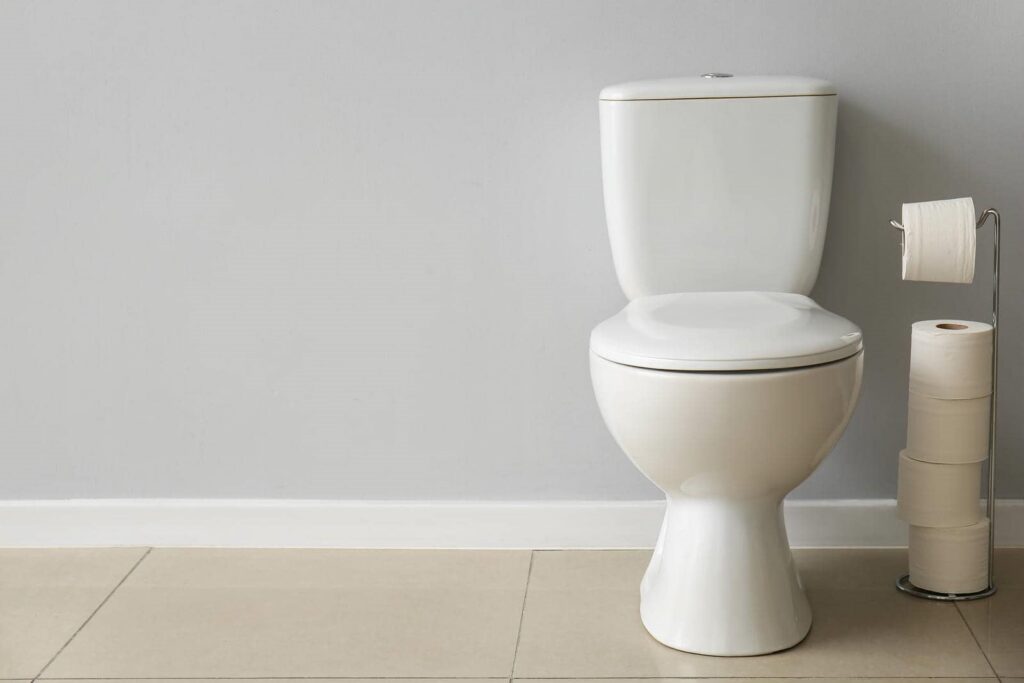 White toilet with a stand holding multiple rolls of toilet paper against a gray wall.