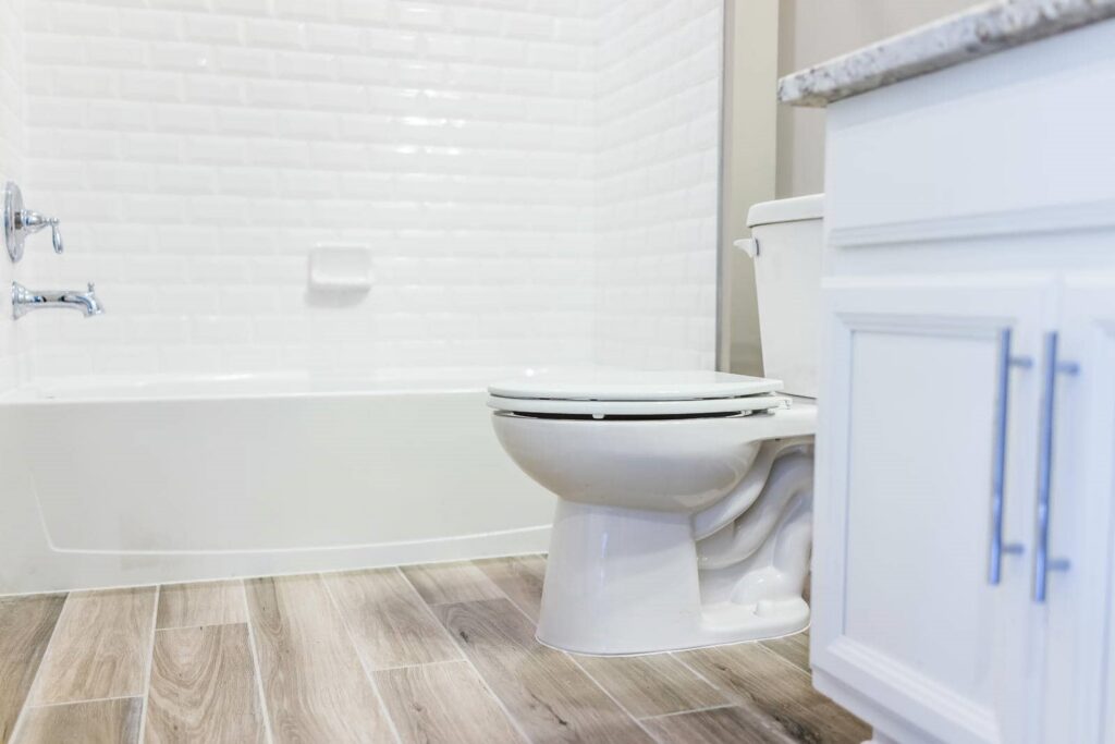 White toilet with closed lid next to a white cabinet and bathtub with white tiled walls.