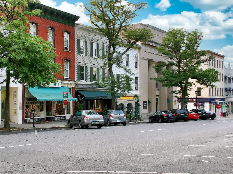 Street view of parked cars along a row of colorful historic buildings with trees and a blue sky.