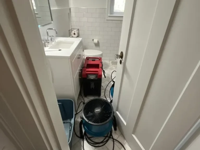 Drying equipment and fans set up inside a small bathroom with white tiles and fixtures.