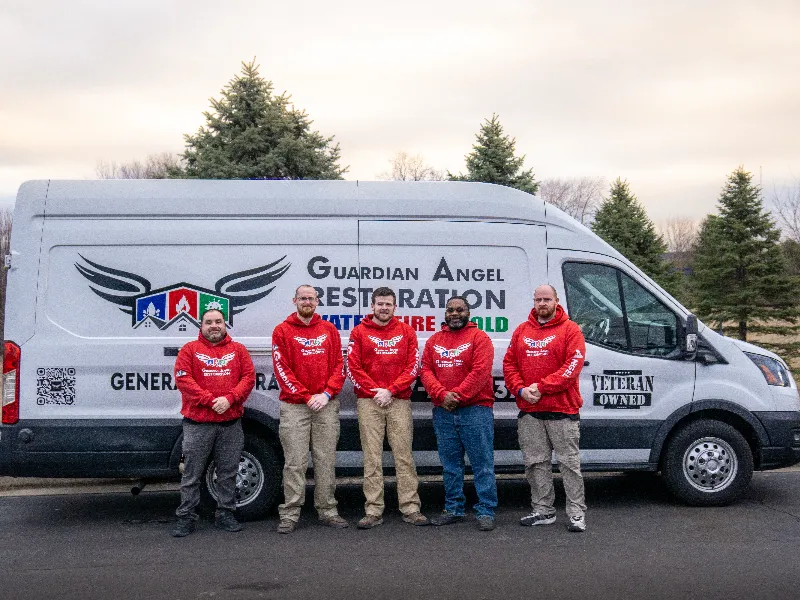 Five men in red hoodies stand in front of a white van with "Guardian Angel Restoration" branding.