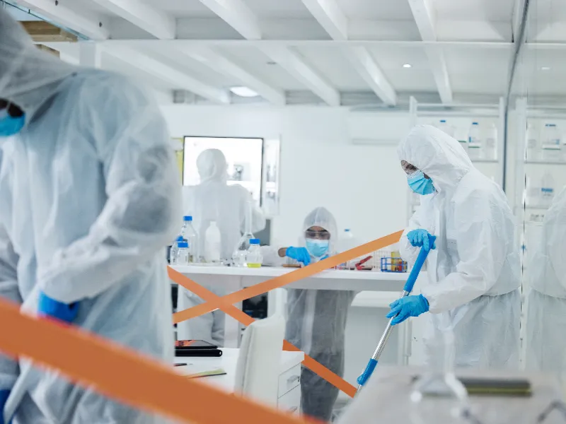 Scientists in full protective suits and masks working in a laboratory with orange tape barriers.