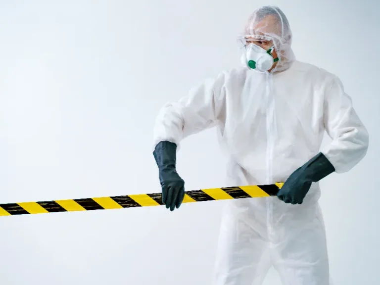 Person in protective suit and mask holding yellow and black caution tape.