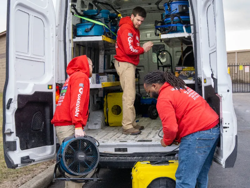 Three men in red hoodies loading equipment into a white van with open rear doors.