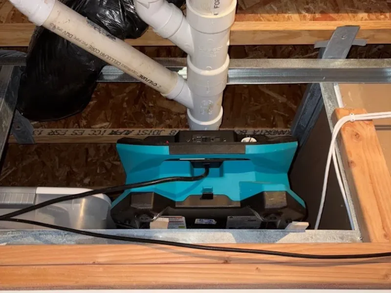 Blue and black power tool connected to pipes inside a wooden and metal frame.