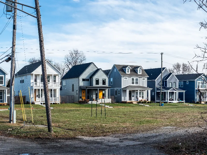 Row of modern two-story houses with front porches and a grassy lawn under a partly cloudy sky.