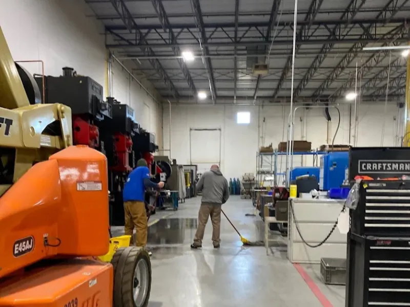 Two workers clean the floor inside a large industrial warehouse.