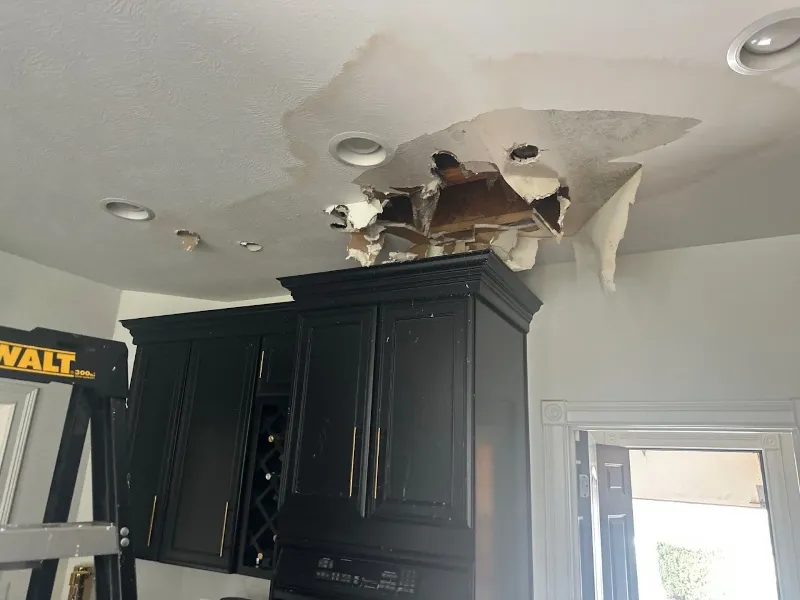 Ceiling with large water damage and a hole above kitchen cabinets.